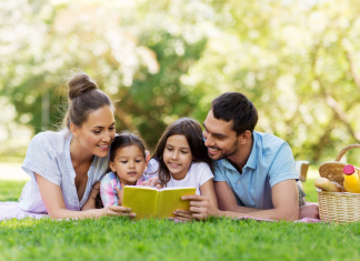 Cultivate Connection with your Kids: 8 Simple, Low-Cost Ideas a mom and dad with their two young kids laying in the grass as they build community by reading a book together