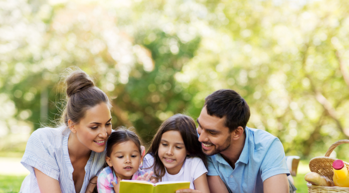 a mom and dad with their two young kids laying in the grass as they build community by reading a book together