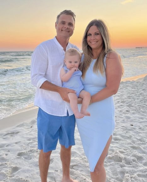 a man and a woman standing on the beach, holding a baby boy that was conceived through infertility treatments