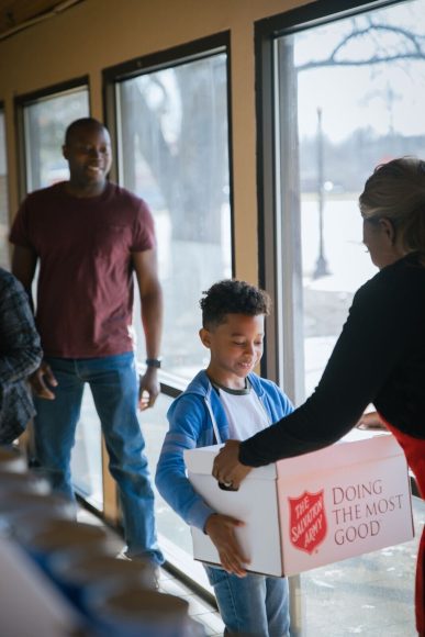 an African American father looks on as his son shares Salvation Army donations with a volunteer