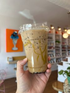a hand holding an iced coffee in the forefront, and the interior of a small business in the background