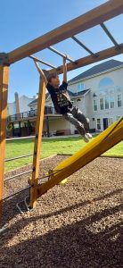 young boy climbing on the monkey bars in his backyard playground with a yellow slide