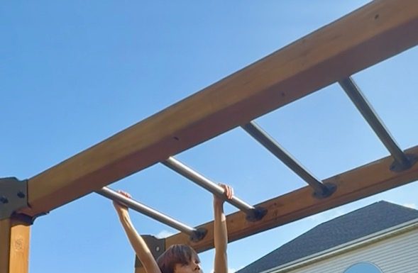 No More Monkey Business: Monkey Bars, Broken Bones and Mom Guilt young boy climbing on the monkey bars in his backyard playground with a yellow slide