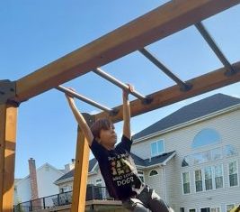 young boy climbing on the monkey bars in his backyard playground with a yellow slide