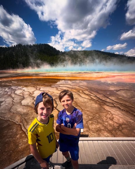 two boys standing in front of a geyser at Yellowstone, one of the National Parks