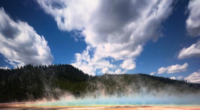 two boys standing in front of a geyser in Yellowstone, one of the National Parks