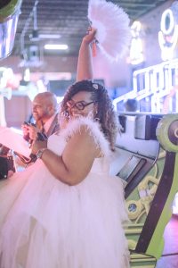 a woman in a white dress sitting in front of an arcade game at her vow renewal celebration