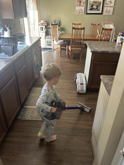 a young boy doing chores as he vacuums the kitchen floor