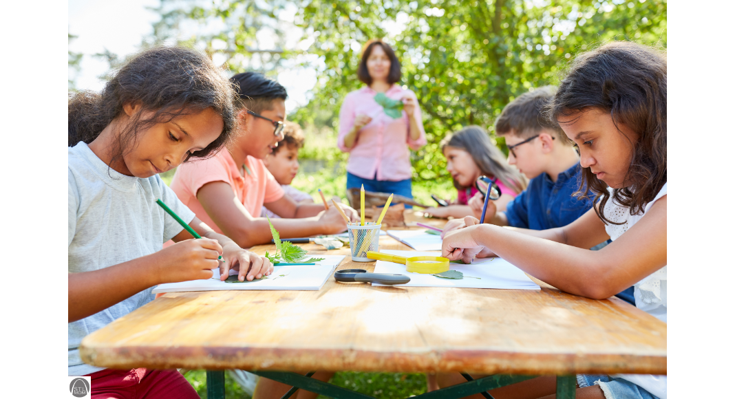 kids at a summer camp, sitting at a table, doing crafts while the camp counselor looks on