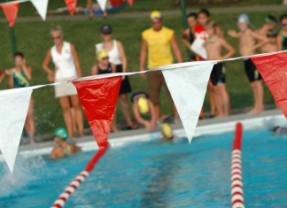 Tips from a Swim Mom a pool with lane lines and flags hanging over it, with kids ready to dive in for a swim meet