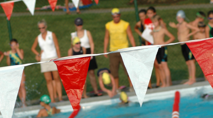 Tips from a Swim Mom a pool with lane lines and flags hanging over it, with kids ready to dive in for a swim meet