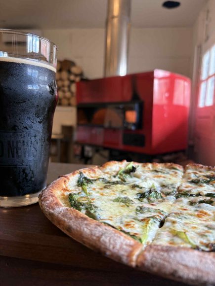 pizza and beer in the foreground, and a pizza oven in the background