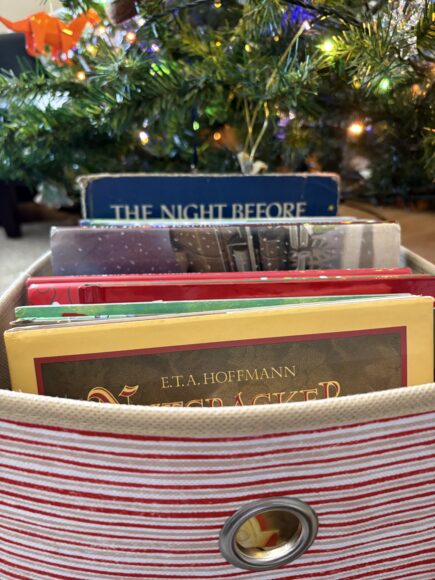 A candy-cane striped box of books under a Christmas tree.