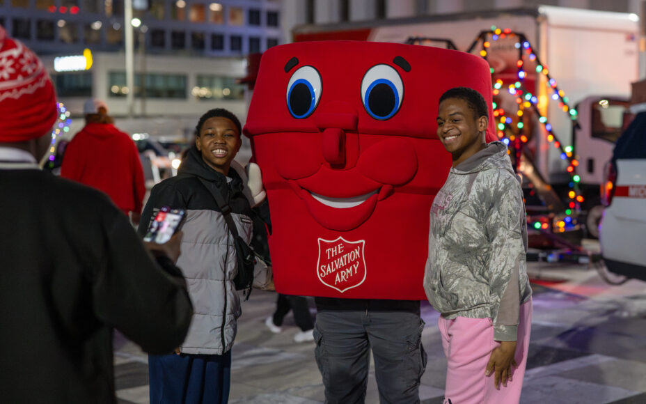 a man and a woman standing next to a mascot in a Salvation Army red kettle costume at a volunteering event in St. Louis