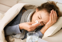 You Want Me to … Rest? a woman under a blanket on the couch holding a tissue to her nose. on the table beside her sits medicine and a glass of water