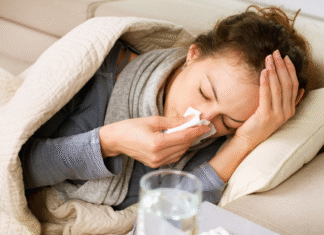 You Want Me to … Rest? a woman under a blanket on the couch holding a tissue to her nose. on the table beside her sits medicine and a glass of water